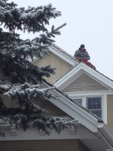 Man installing Christmas lights on a snowy roof.
